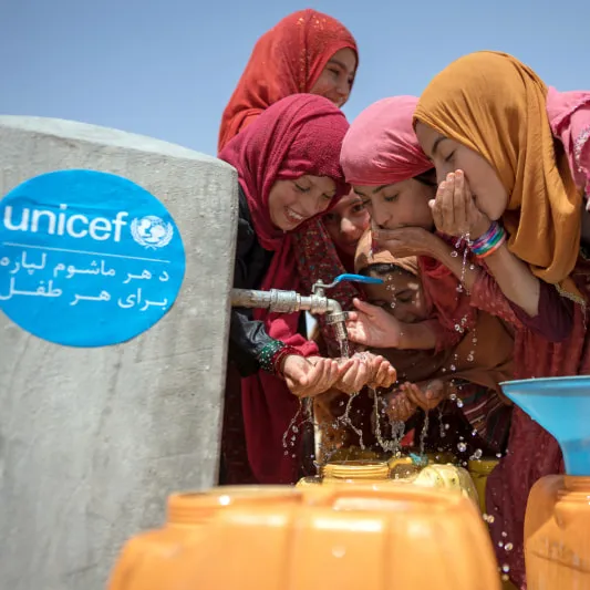 Four people in colorful clothing drink clean water from a tap