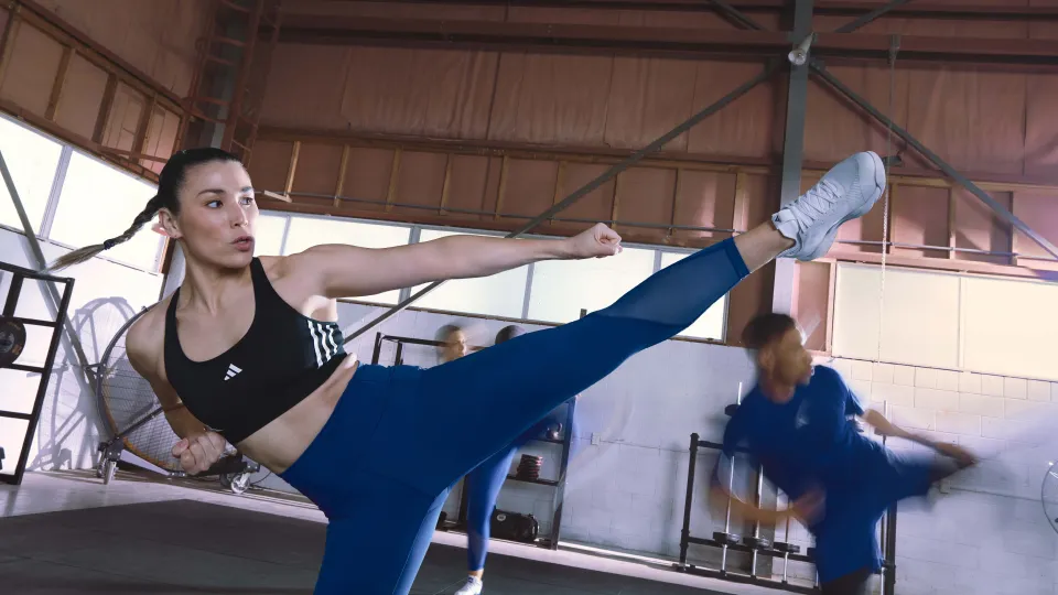 A women in adidas crop top and tights doing a side kick in a group exercise studio.